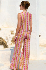 Woman wearing a colorful patterned jumpsuit standing against a white wall.