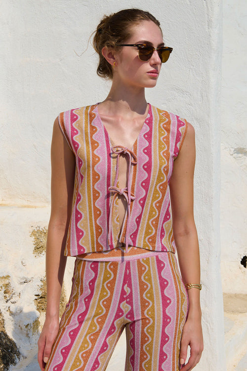 Woman wearing a colorful patterned outfit against a white wall.